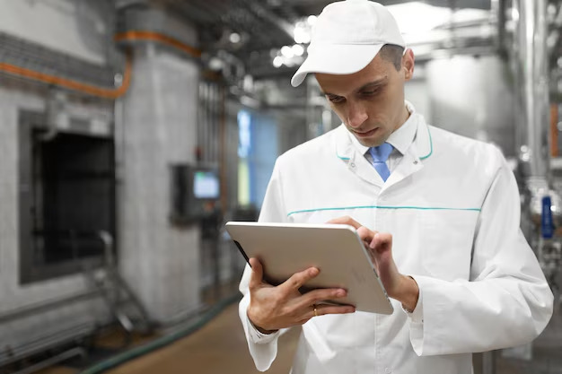 Técnico con casco de seguridad revisando diagrama de Gantt en tablet en planta de construcciones metálicas.